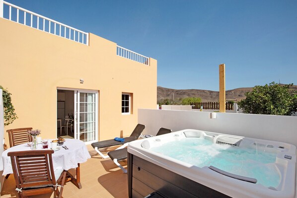 Un patio en la azotea con un jacuzzi, sillones de descanso y una mesa de comedor con sillas.