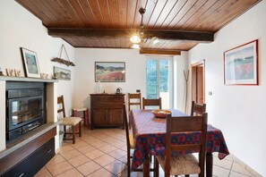 A dining area with a table set for two, wooden chairs, a wooden ceiling, and a window with a view.