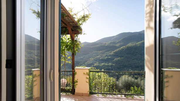 A balcony with a view of a mountainous landscape, a pergola, and a tiled floor.