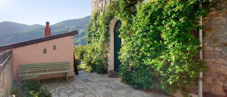 Un camino de piedra que lleva a un edificio con una puerta verde, un banco y vistas a montañas.