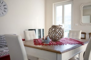 Un coin repas avec une table en bois, des chaises blanches, un élément décoratif en fibres tressées et une horloge murale.