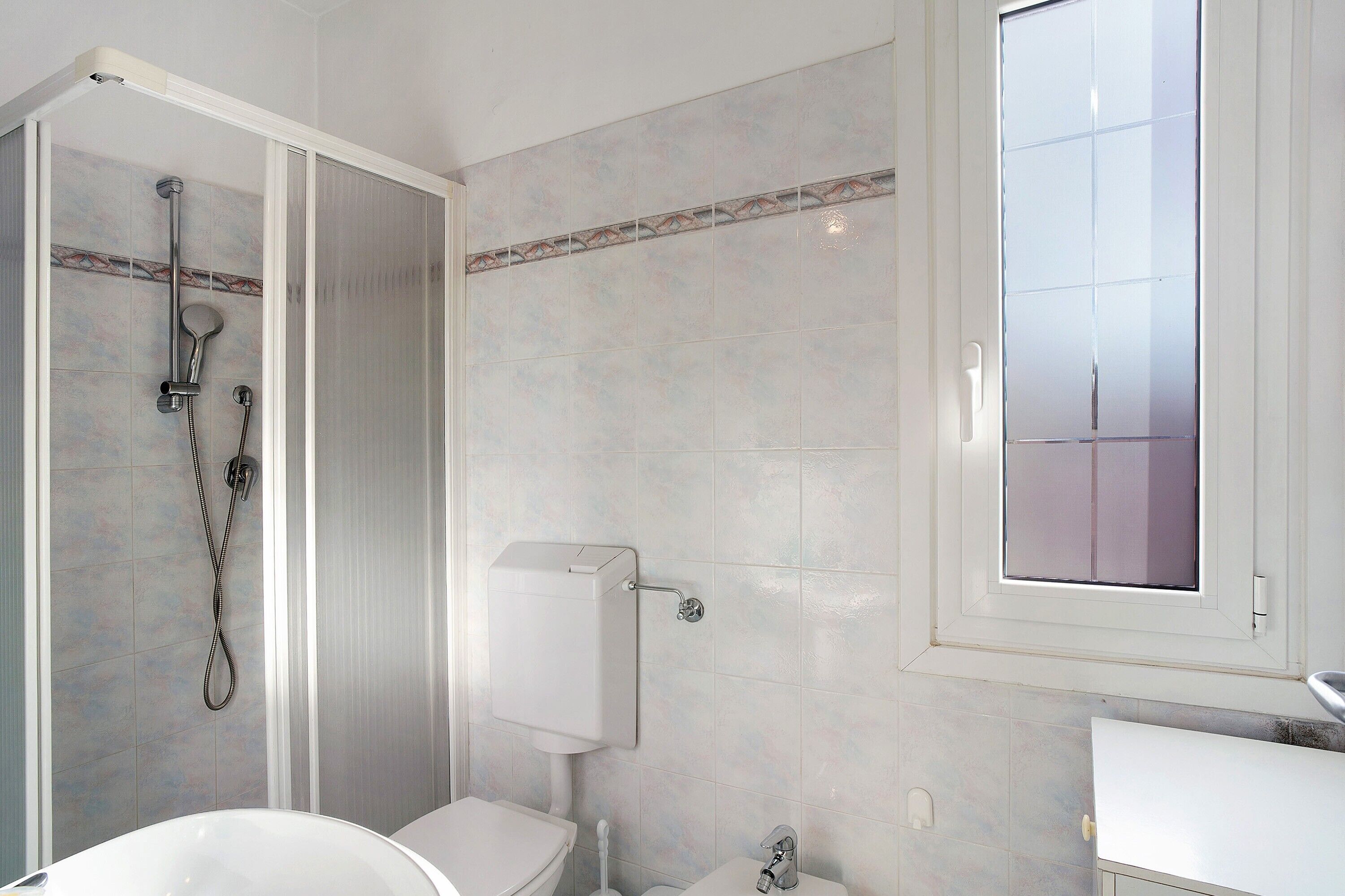 Een badkamer met douche, toilet, wastafel en raam.