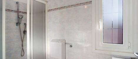 Een badkamer met douche, toilet, wastafel en raam.