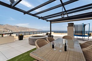 An outdoor patio with wicker furniture, a glass table, and a view of the sea.