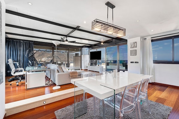 A modern living space with a dining area, a sofa, a desk, and a large window offering a view.