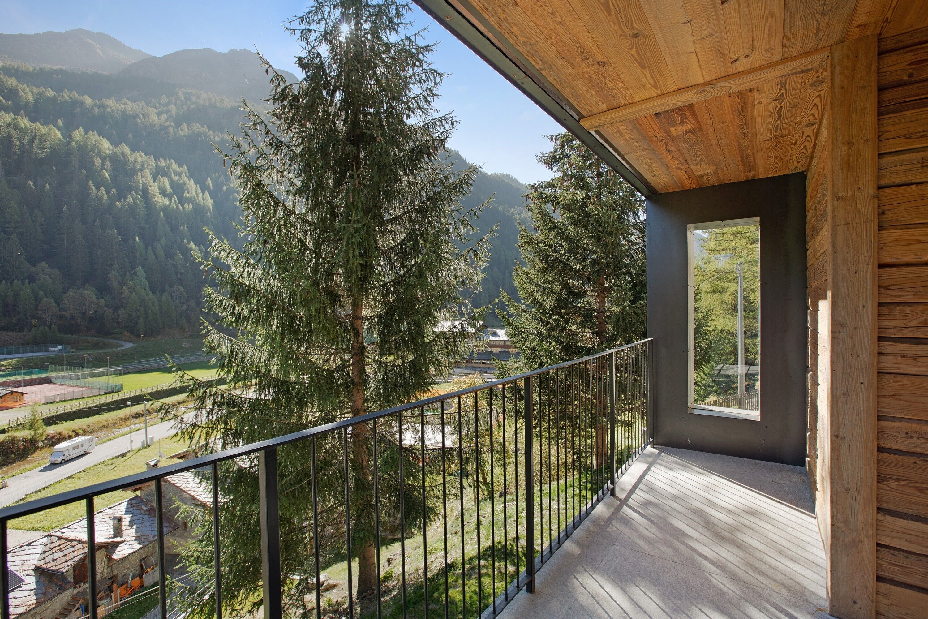 Ein Balkon mit Holzwertung, Blick auf ein bewaldetes Tal und ein Gebirge in der Ferne.