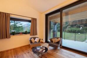 A room with two chairs, a small table, and a large window with a view of a forested area.