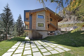A modern multi-story house with a stone facade, wooden accents, and a stone pathway leading to the entrance.