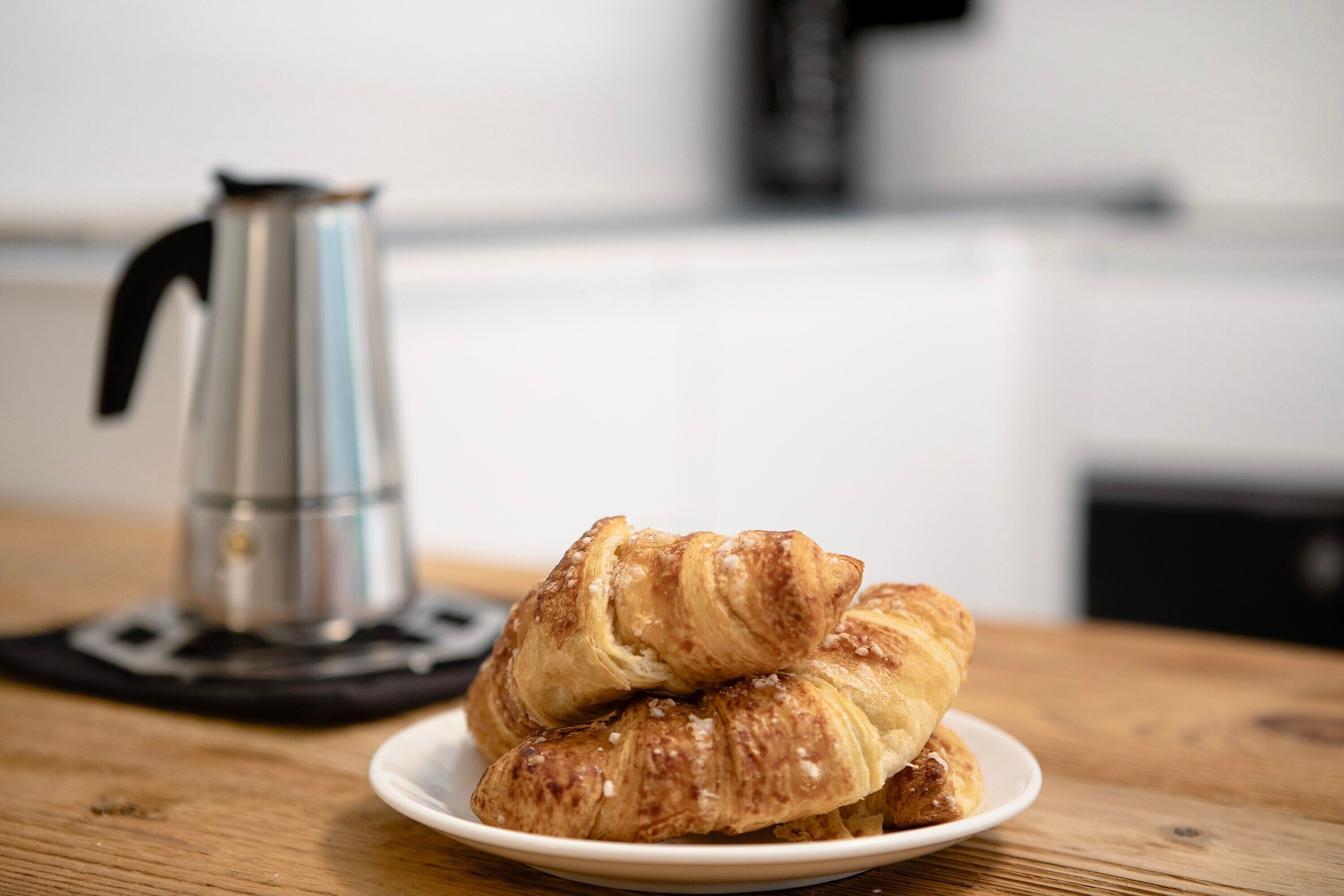 Un plato con croissants y una cafetera sobre una mesa de madera.