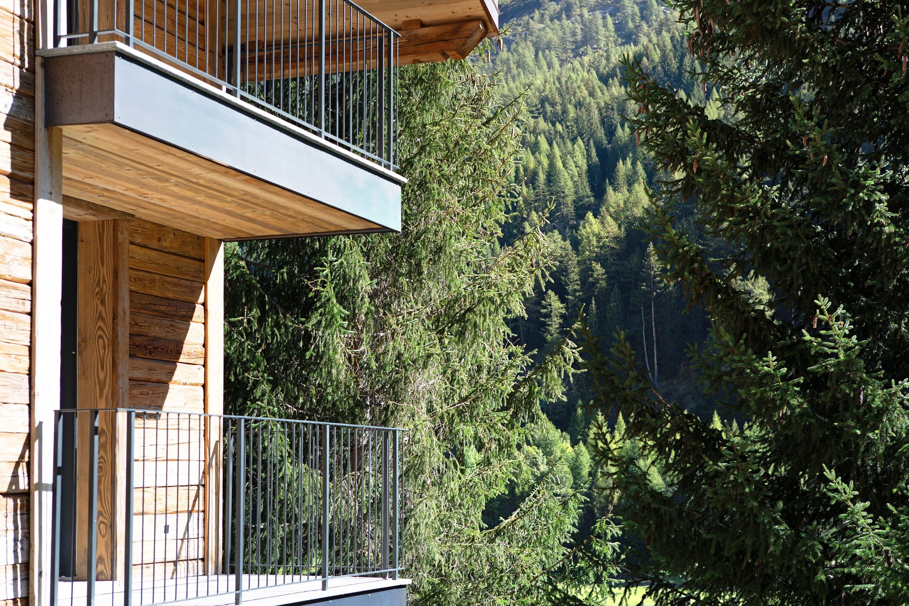 A wooden cabin with a balcony overlooking a forested mountain.