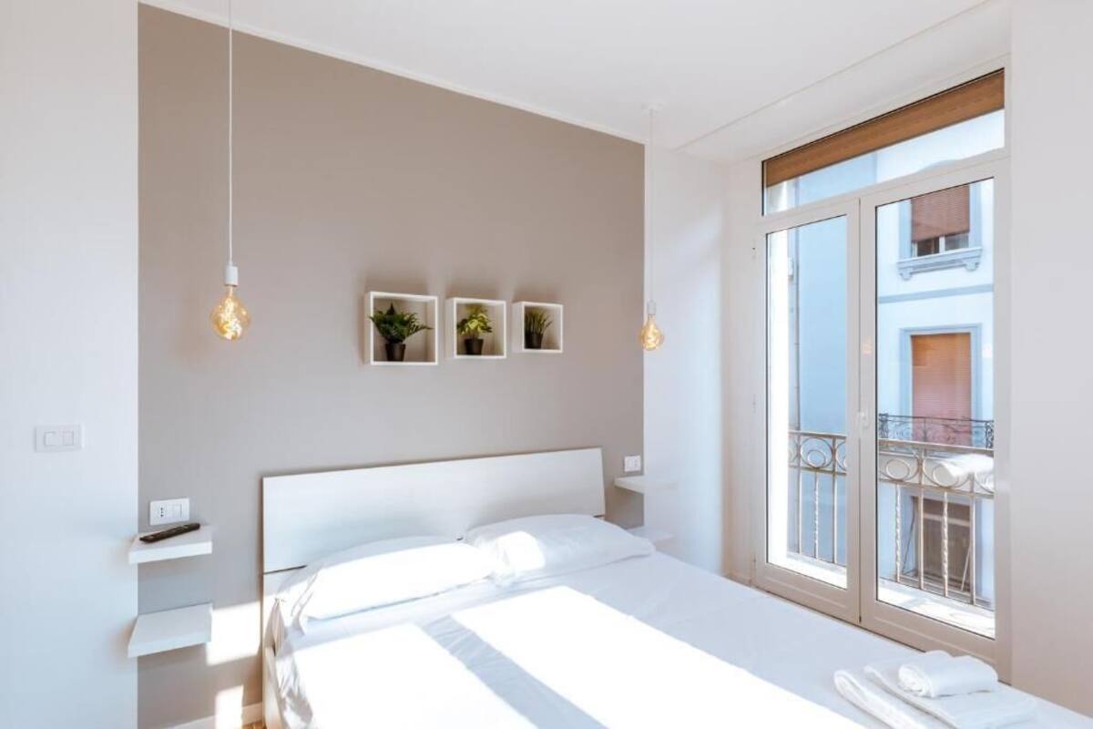 Moderni hotellihuone, jossa on suuri sänky, parveke, jolta on näkymä, ja seinällä kolme ruukussa olevaa kasvia.