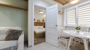Un dormitorio moderno con techo de madera, una puerta blanca que da al baño, una cama blanca y un área de comedor con mesa y sillas.