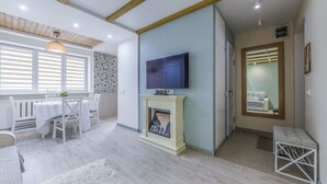 Una sala de estar moderna con chimenea, un comedor con mesa y sillas blancas, y un televisor montado en la pared.