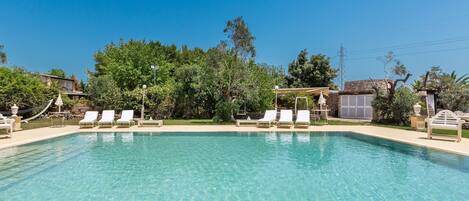 A clear swimming pool with white lounge chairs and a pergola.