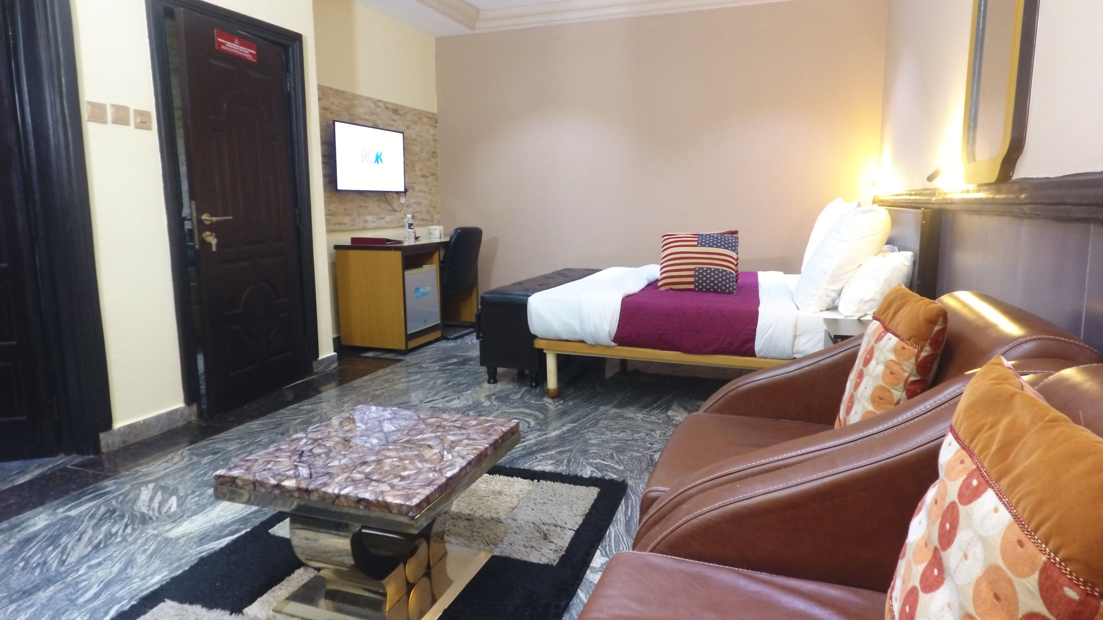 Een hotelkamer met een bed, een leren bank, een kleine tafel, een bureau en een televisie aan de muur.
