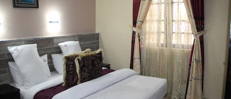 Una cama bien hecha con ropa de cama blanca y burdeos, un cabecero con panel gris y una almohada decorativa.