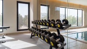 A gym with weightlifting equipment, large windows, and a pool. - Alenwan Serviced Apartments (Al Khobar)
