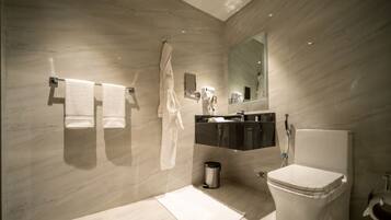 Un baño moderno con piso de mármol, inodoro blanco, tocador negro, espejo y dos toallas colgadas en la pared.