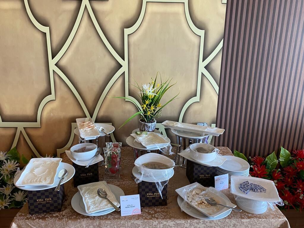 Una barra de buffet con varios platos y recipientes identificados con 'Villa Park' sobre una mesa.