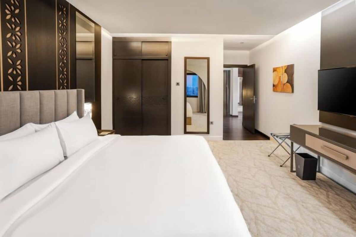 A hotel room with a large bed, a TV, a desk, and a wardrobe.