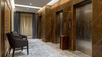 A modern elevator area with marble walls, a black upholstered chair, and a patterned carpet.