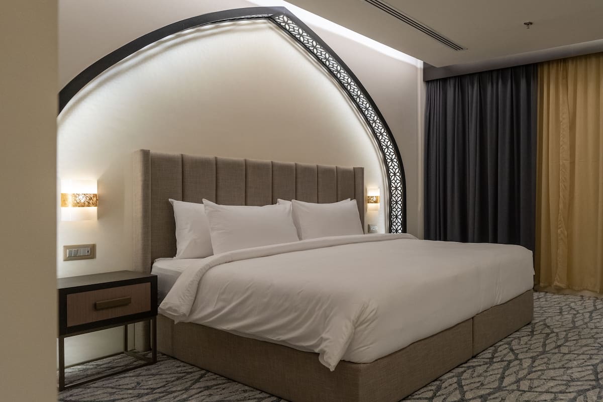 Une chambre d’hôtel moderne avec un grand lit, une table de chevet et une arche décorative sur le mur.