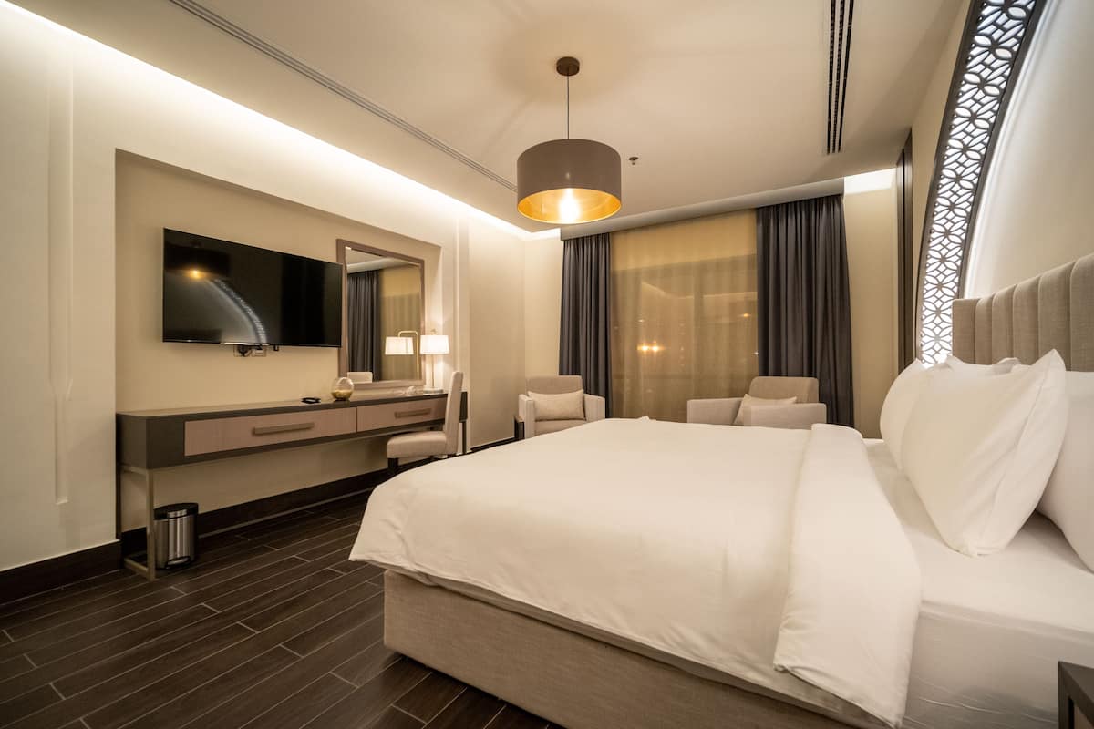 Une chambre d’hôtel moderne dotée d’un grand lit, d’une télévision à écran plat, d’un bureau avec une chaise et d’une salle de bain avec un miroir et un meuble-lavabo.