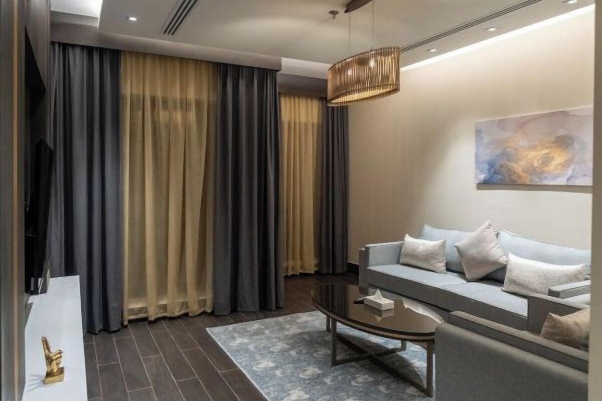 A modern living room with a sofa, a coffee table, and a large window with curtains.