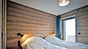 A bedroom with a wooden wall, a bed with white bedding, a bedside lamp, and a window with curtains.