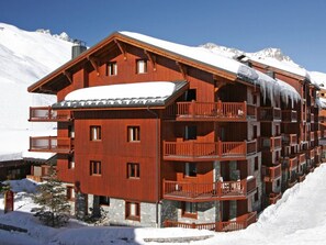 A multi-story wooden building with balconies, set against a snowy mountain backdrop. - Comfortable apartment with terrace and WIFI - 6 pers (Tignes)