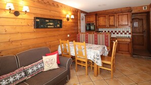 A cozy room with a wooden sofa, a dining table with chairs, a kitchen area with wooden cabinets, and wall-mounted lamps. - Comfortable apartment with terrace and WIFI - 6 pers (Tignes)