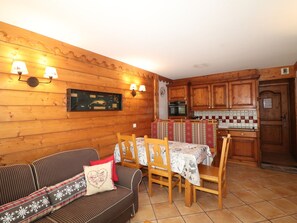 A cozy room with a wooden sofa, a dining table with chairs, a kitchen area with wooden cabinets, and wall-mounted lamps. - Comfortable apartment with terrace and WIFI - 6 pers (Tignes)