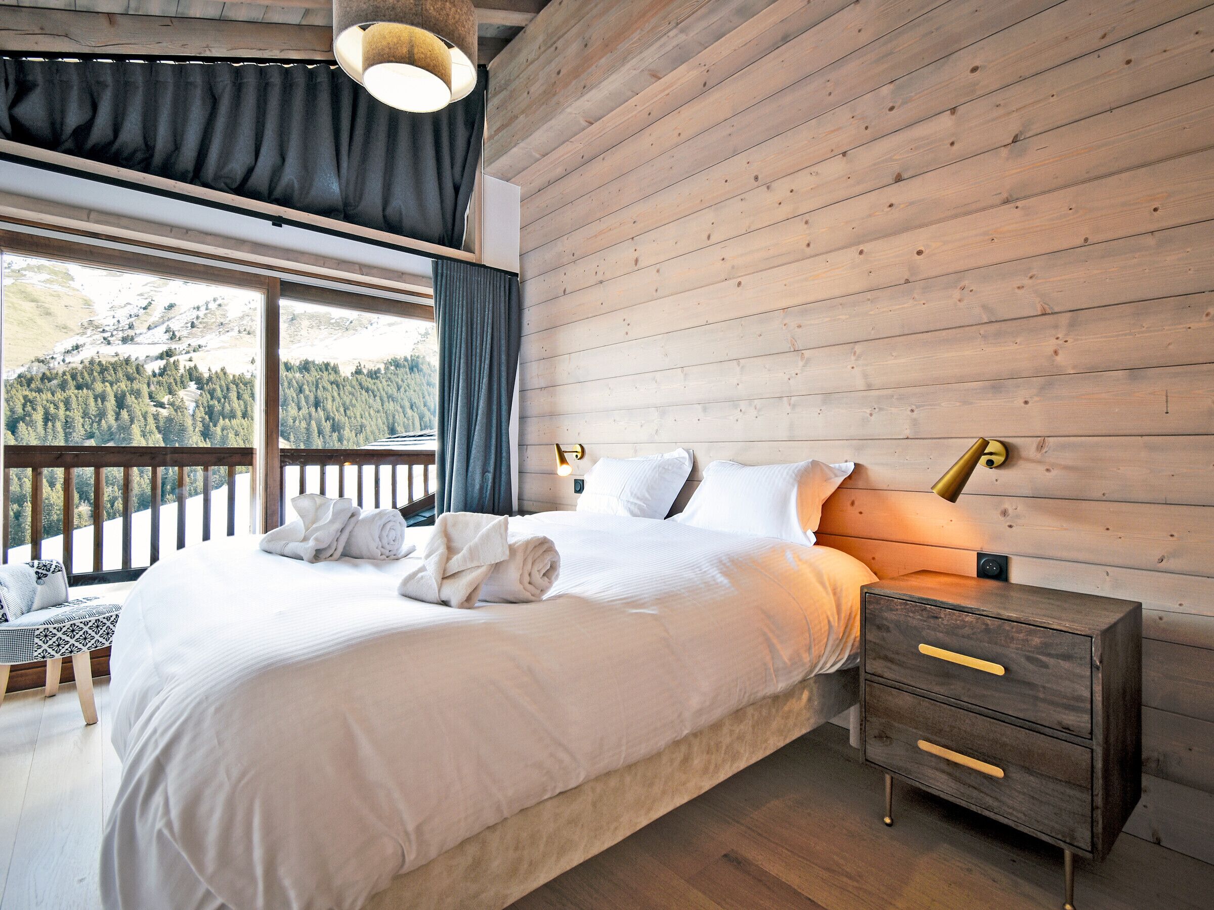 A bedroom with a large bed, wooden headboard, bedside tables, and a view of a mountainous landscape.