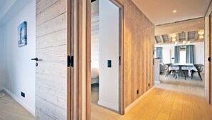 A modern interior with wooden panel walls, a dining area with a table and chairs, and a visible bed in the background.