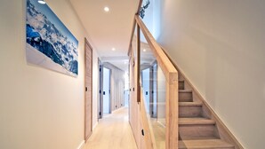 A modern hallway with wooden flooring, a glass railing staircase, and a mountain landscape painting on the wall.