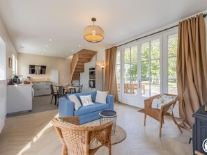 A spacious living area with a blue sofa, wicker chairs, a dining table, and a kitchen in the background. - House with garden, fireplace, wifi and pets welcome (Rethondes)