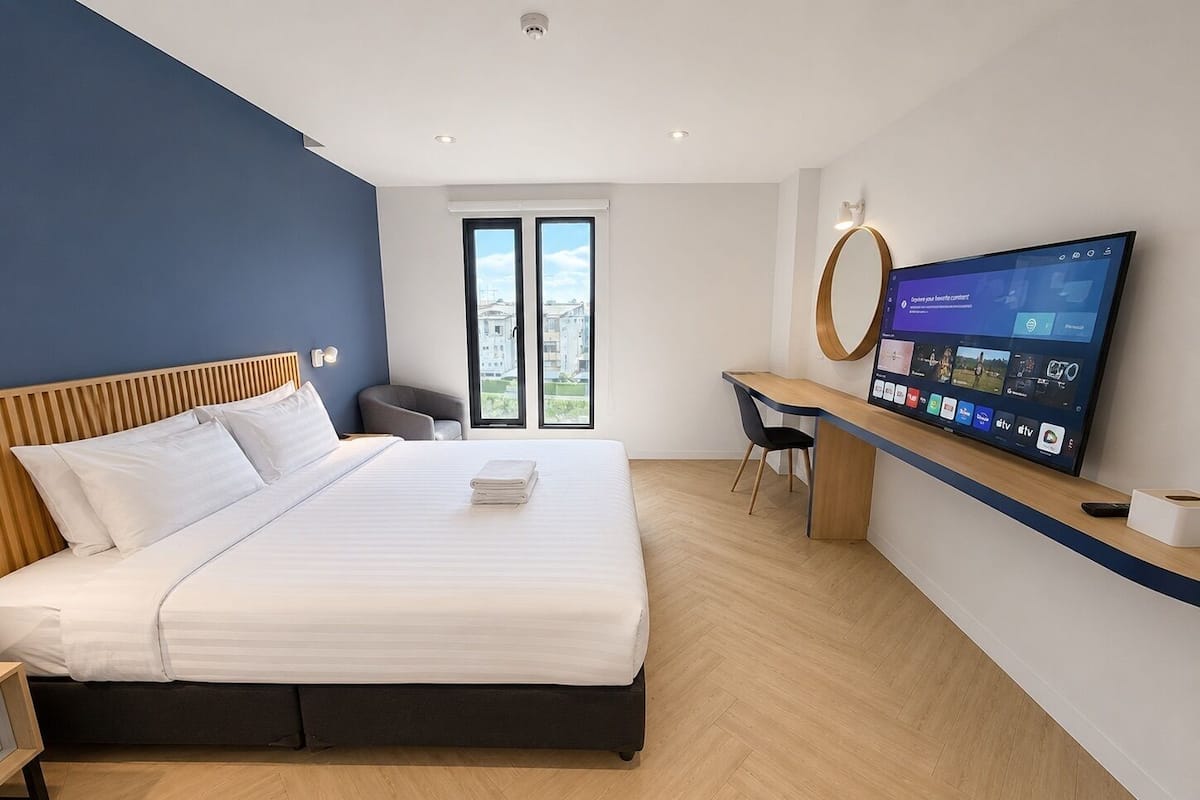 Quarto de hotel moderno com cama, escrivaninha, TV e vista para a cidade.