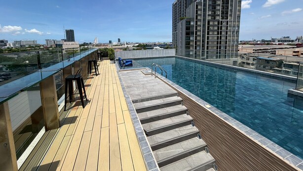 Una piscina en la azotea con vistas despejadas del horizonte urbano, una terraza de madera y un edificio moderno al fondo.