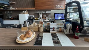 Interior de una cafetería con mostrador de madera, cartel de menú y máquina de café.