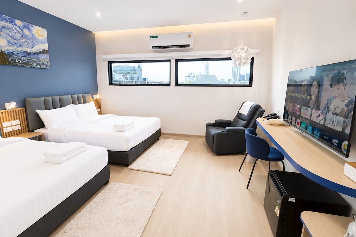 Quarto de hotel com duas camas, uma escrivaninha com computador, televisão e uma cadeira de massagem.