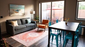 A living room with a gray sofa, orange chair, teal chairs, a wooden table, and a painting of a boat on the wall. - Modern State Unit 2 (Traverse City)
