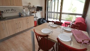 A cozy kitchen with wooden cabinets, a dining table set for four, and a large window overlooking a deck. - Cozy studio near slopes with private garage (Les Gets)