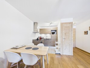 A compact kitchen with modern appliances, a dining area with a table and chairs, and a wooden door.