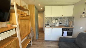 A compact living space with a kitchenette, a flat-screen TV mounted on a wooden wall, and a grey sofa.