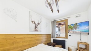 Ein Schlafzimmer mit Holz-Kopfteil, einem Bett mit weißer Bettwäsche, einem angebrachten Fernseher und einem Wandbild von Geweihen.