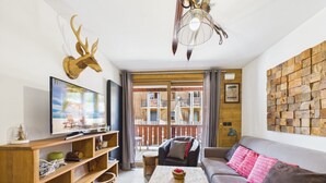 Ein Wohnzimmer mit Fernseher, Holzböden, einer Couch, einem Couchtisch und einem Balkon mit Holzgeländern.