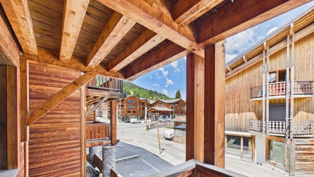Ein Holzhaus mit Balkon, Steinpfeilern und Blick auf andere Gebäude und eine Straße.