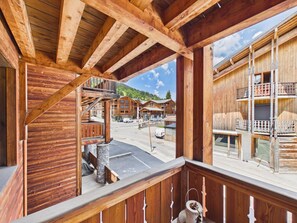A wooden building with a balcony, stone pillars, and a view of other buildings and a road.