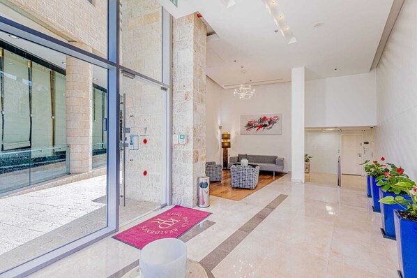 A modern hotel lobby with a reception desk, seating area, and a staircase leading to upper floors.