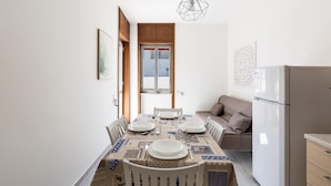 Un comedor con una mesa dispuesta para cuatro personas, un refrigerador y un sofá.
